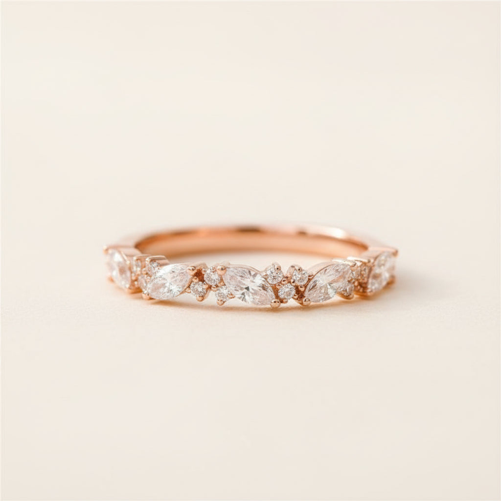 A rose gold eternity ring with marquise-cut and round diamonds, resting on a textured stone surface with a blurred green background.