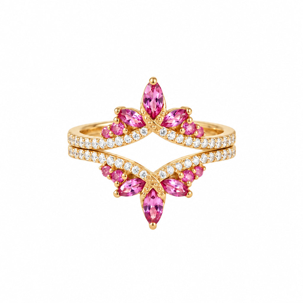 A gold butterfly ring with marquise-cut pink gemstones and pavé-set clear stones, displayed on a textured beige fabric with lace.