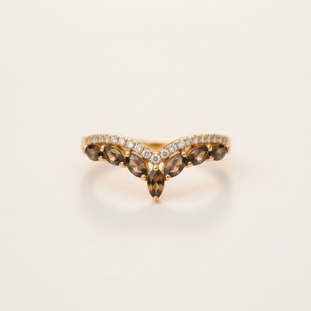 A gold V-shaped ring featuring marquise-cut brown smoky gemstones and a row of small clear stones, resting on a textured stone surface with a blurred green background.