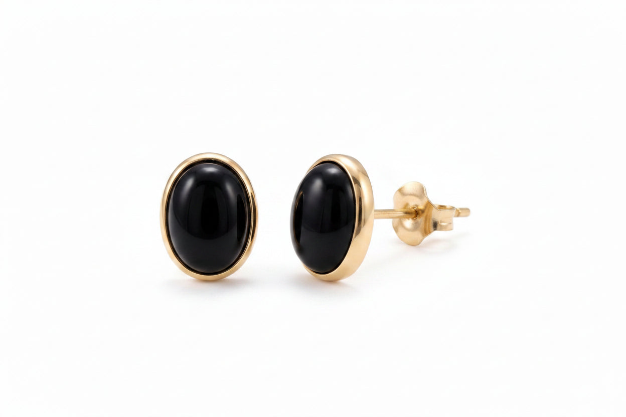A pair of gold oval stud earrings with smooth black cabochon stones, shown on a clean white background.