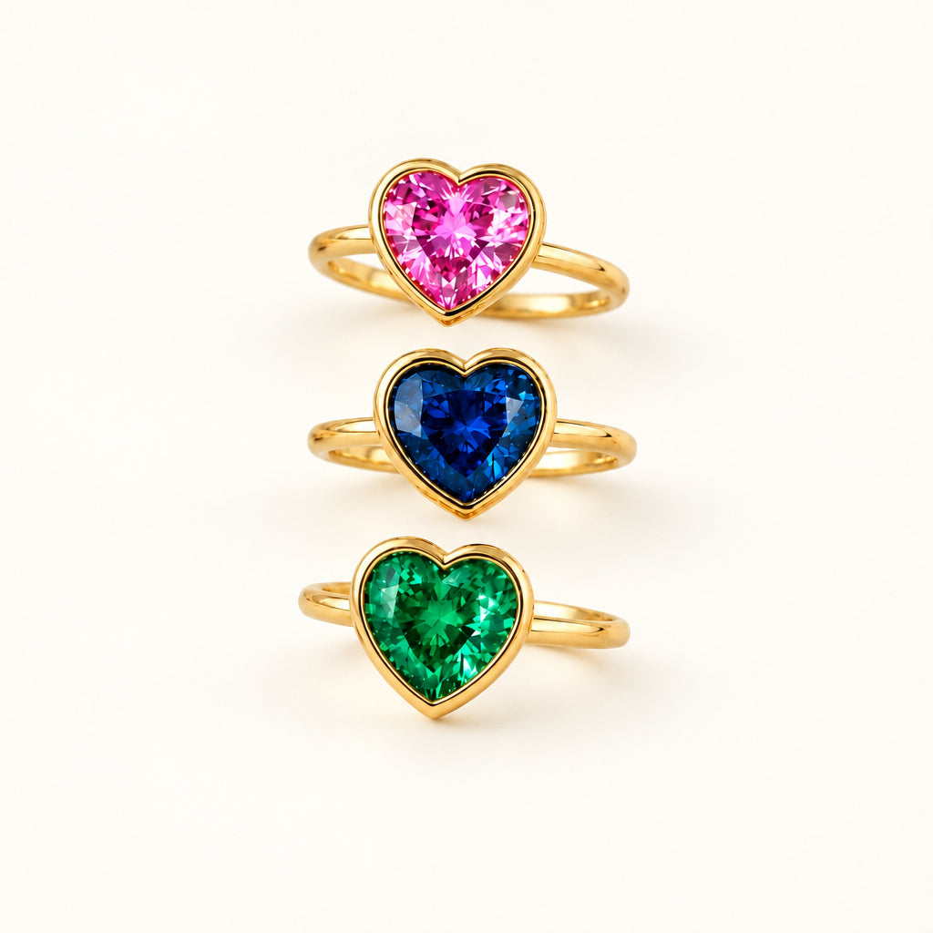Three heart-shaped gemstone rings in pink, blue, and green on a lace fabric background.