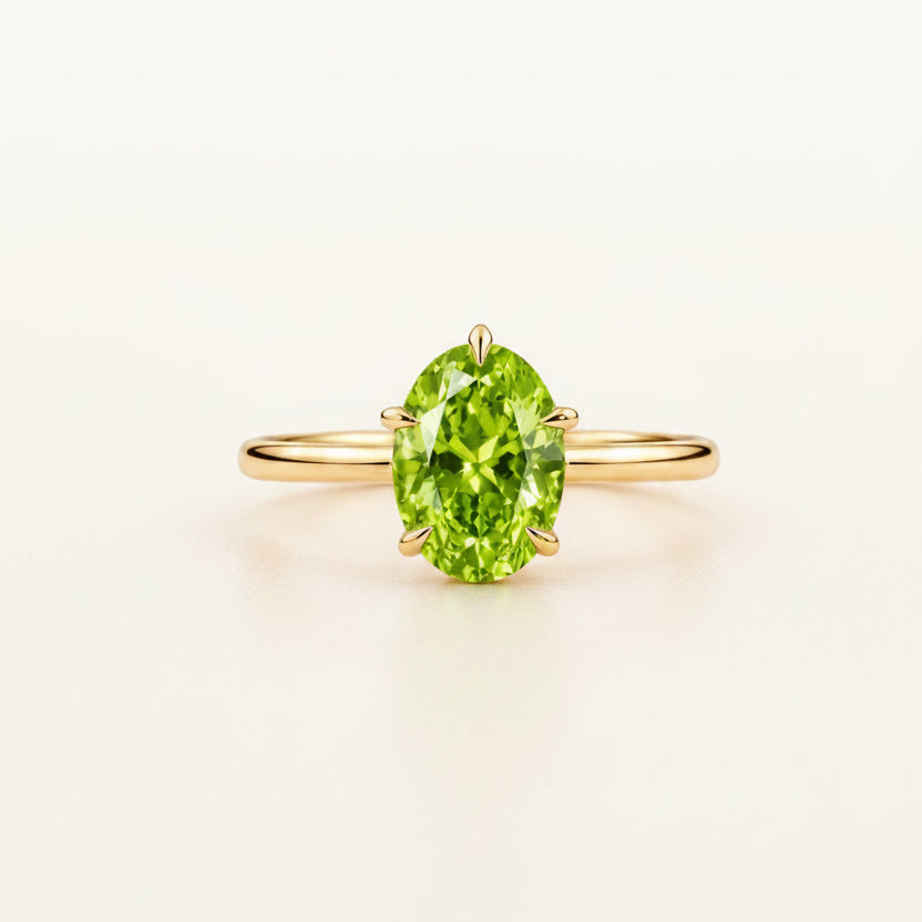 A yellow gold ring featuring a marquise-cut green peridot gemstone, displayed on a white marble block against a clean white background.