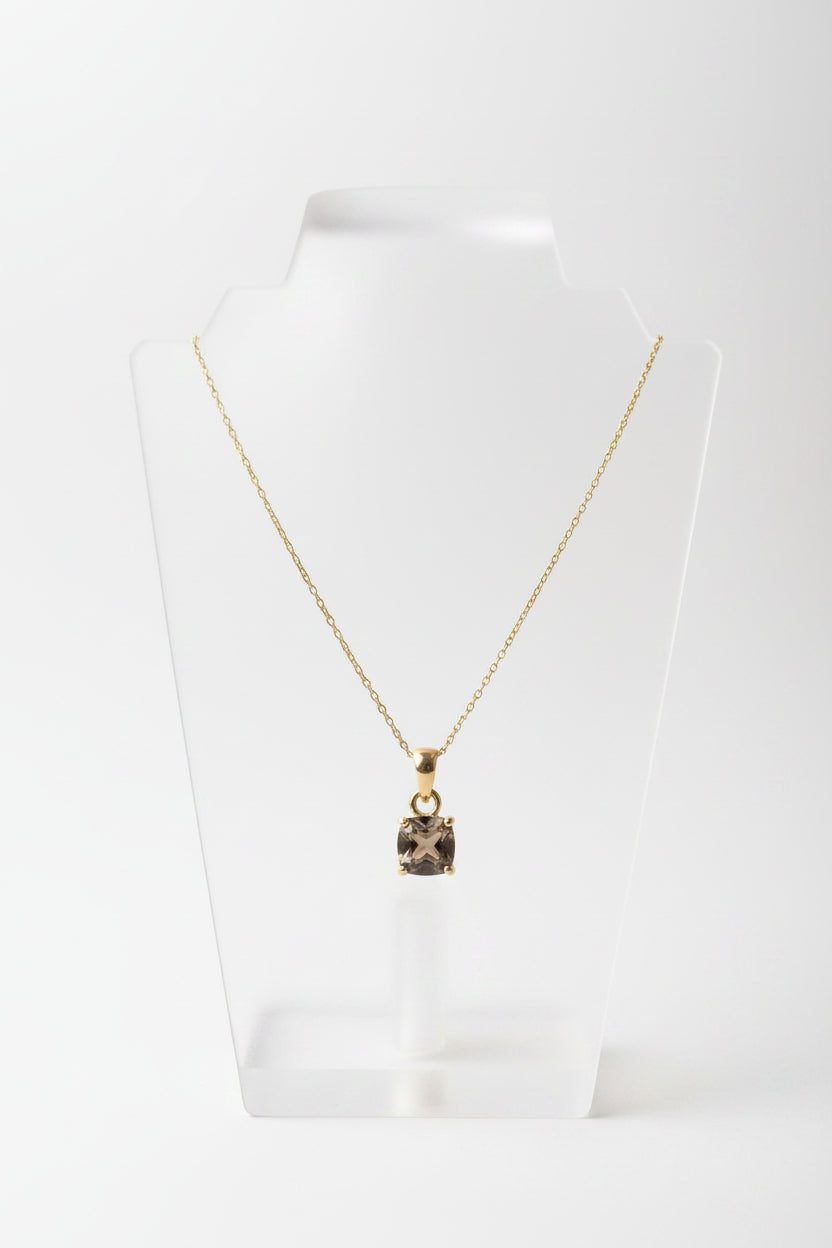 A gold chain necklace with a square dark gray gemstone pendant, displayed on a beige jewelry bust.