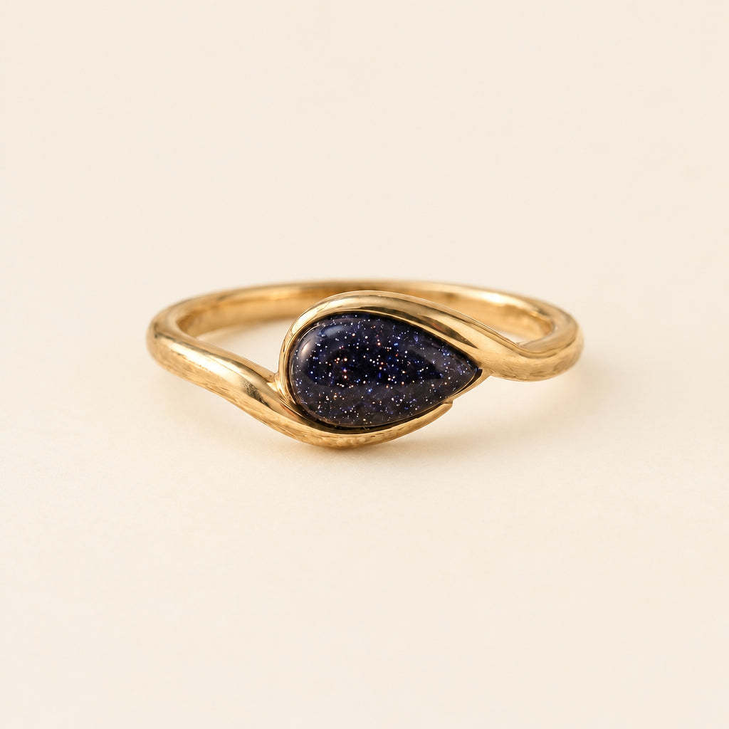 Gold ring with a purple teardrop-shaped stone on a textured fabric background