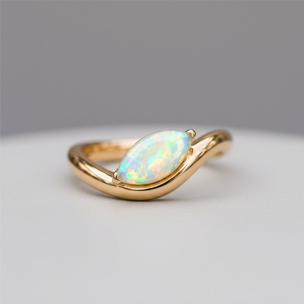 A gold ring with a marquise-cut iridescent opal gemstone, resting on a textured stone surface with a soft-focus natural background.