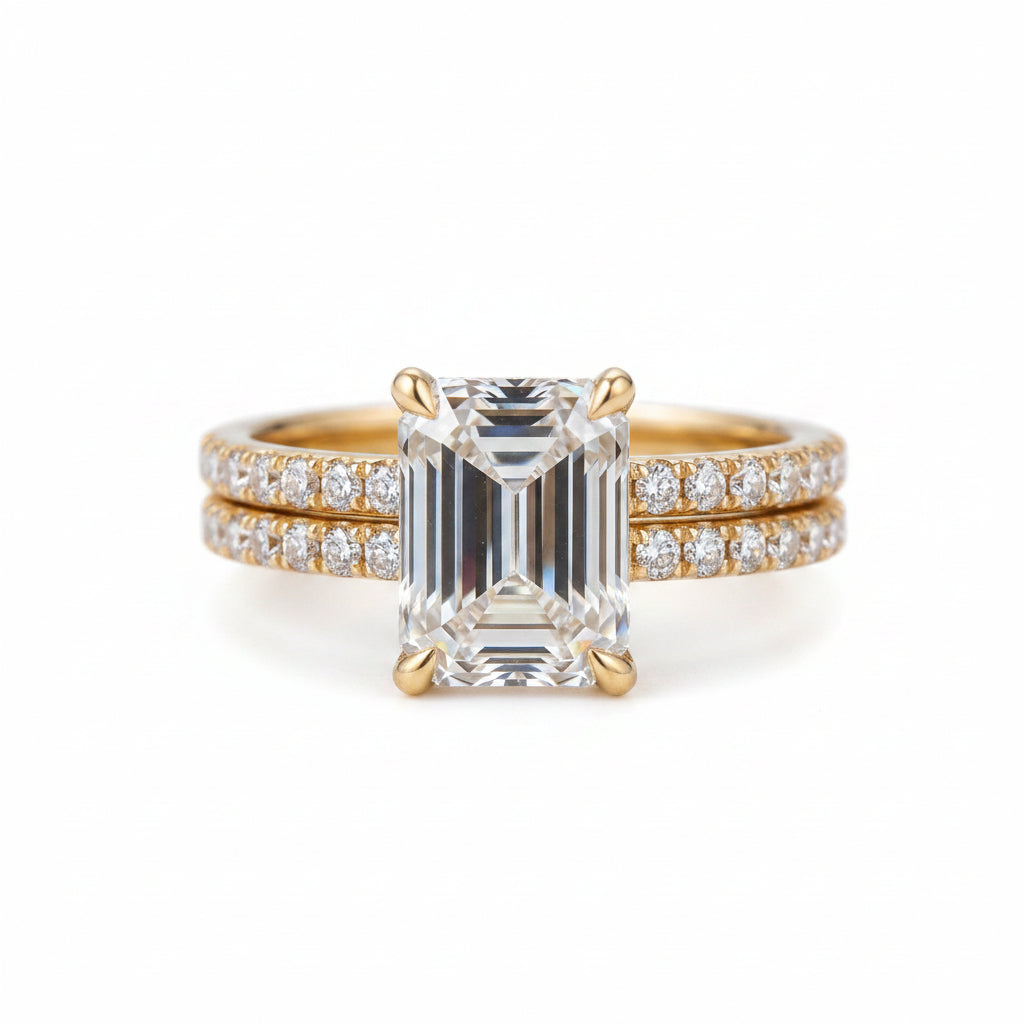 A yellow gold ring set featuring a large emerald-cut clear center stone and a matching double-row pavé band, displayed on a textured black velvet background.