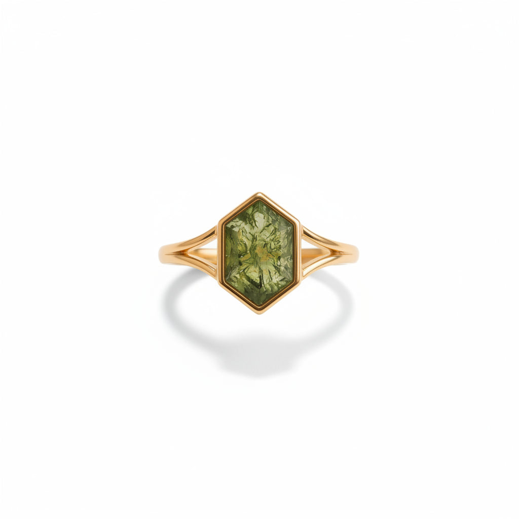 A gold hexagonal ring with a green faceted gemstone, displayed on draped champagne-colored satin fabric.