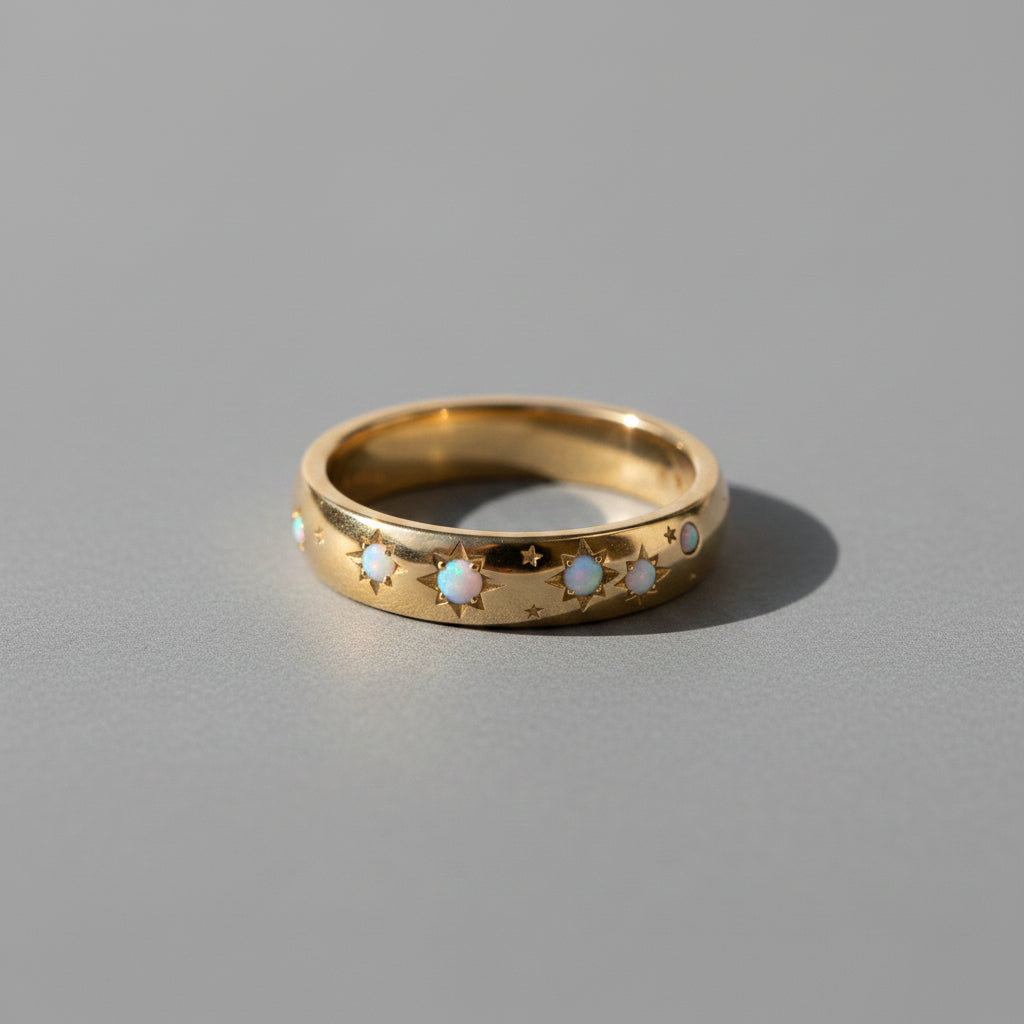 A gold ring with star and moon motifs and small white opal inlays, resting on a textured beige linen surface under warm sunlight.