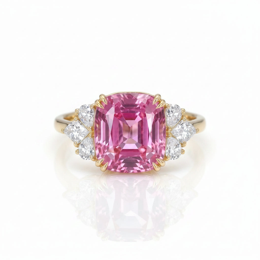 A yellow gold ring featuring a large cushion-cut pink gemstone center, flanked by small clear round and marquise-cut side stones, shown on a dark reflective surface.