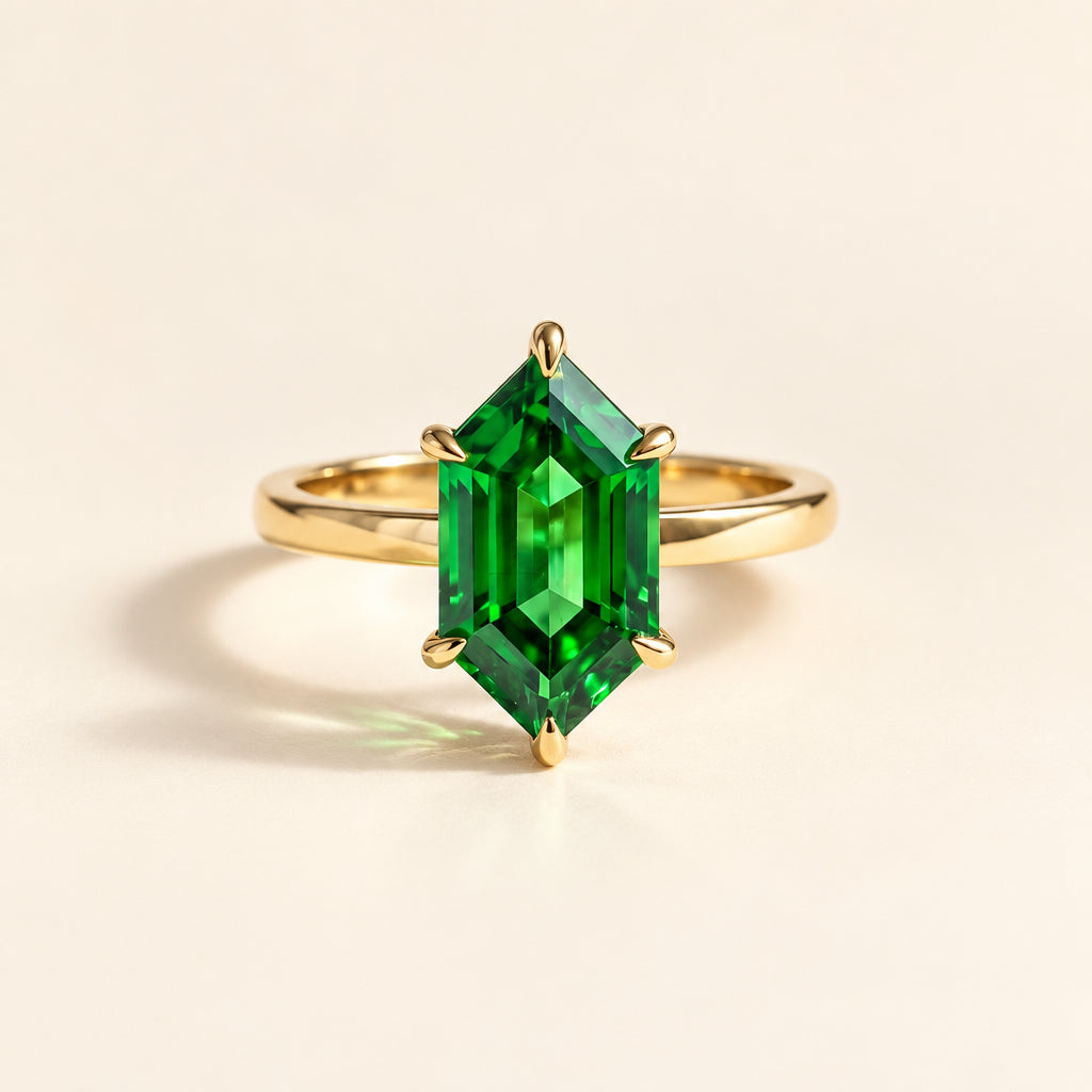 A gold ring with a large emerald-cut green gemstone, styled on a textured cream linen fabric with a lace runner and small dried flowers.