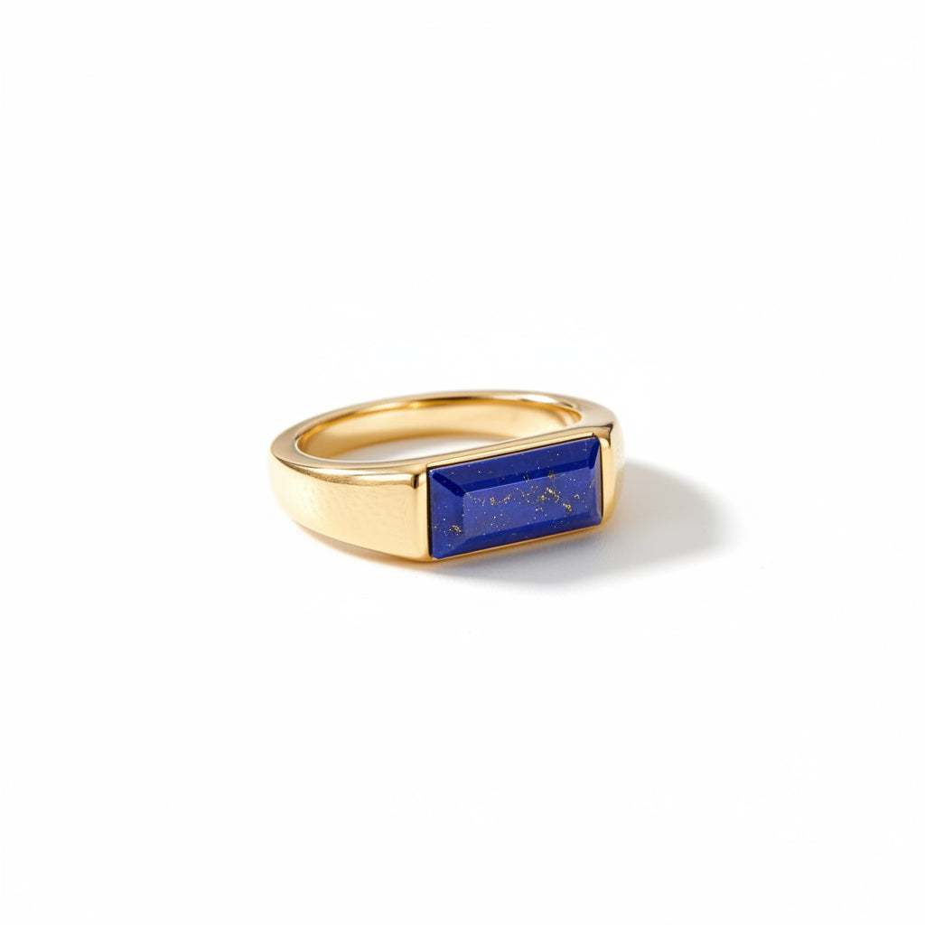 A gold ring with a rectangular blue lapis lazuli stone, resting on a textured beige linen fabric background.