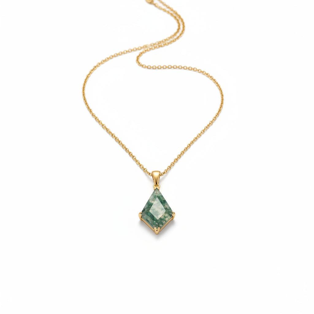 A gold chain necklace with a diamond-shaped green gemstone pendant, displayed on draped cream-colored satin fabric.