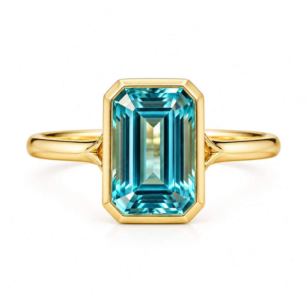 A gold ring with an emerald-cut turquoise gemstone, displayed on a textured beige lace fabric with dried lavender flowers.