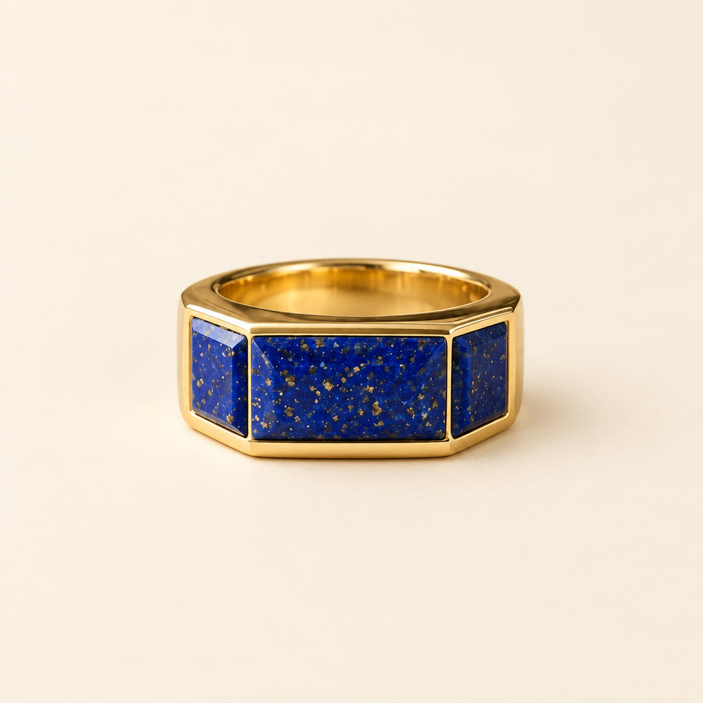 A hexagonal ring with a deep blue lapis lazuli stone inlay and a gold-toned metal setting, resting on an old, open book with printed text.