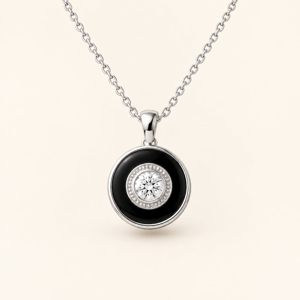 A silver chain necklace with a round pendant displayed on a beige jewelry bust. The pendant features a black circular center with a silver bezel and a clear round gemstone surrounded by a halo of small clear stones.