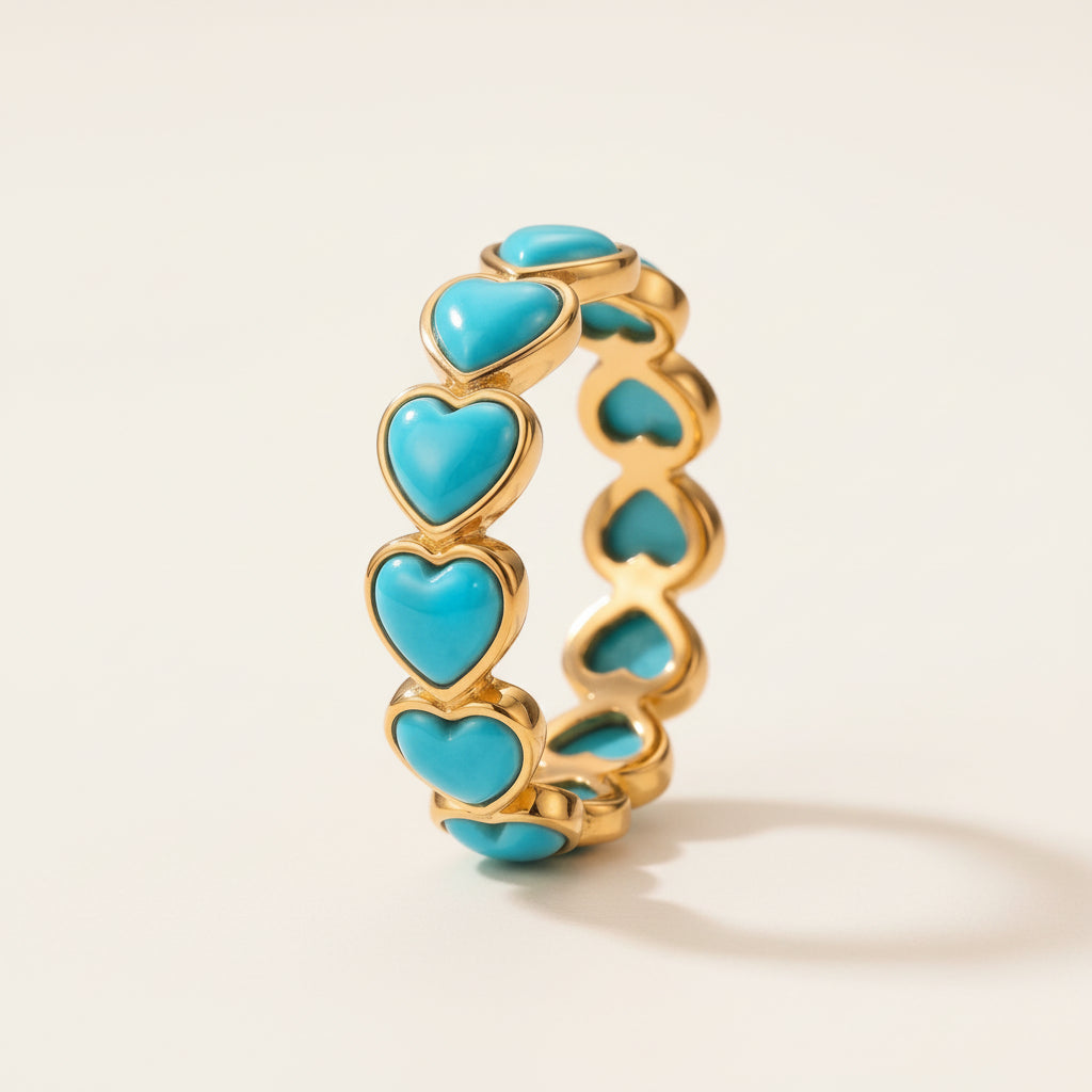 A gold heart-link ring with turquoise heart inlays, resting on a textured stone surface with a soft, blurred natural background.