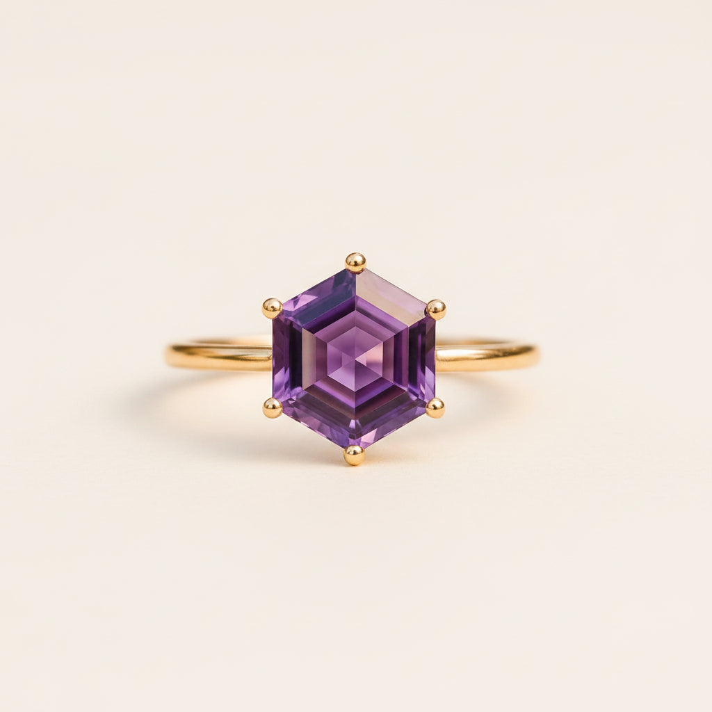 A gold ring with a hexagonal purple amethyst gemstone, resting on a textured wooden surface with a soft-focus natural background.
