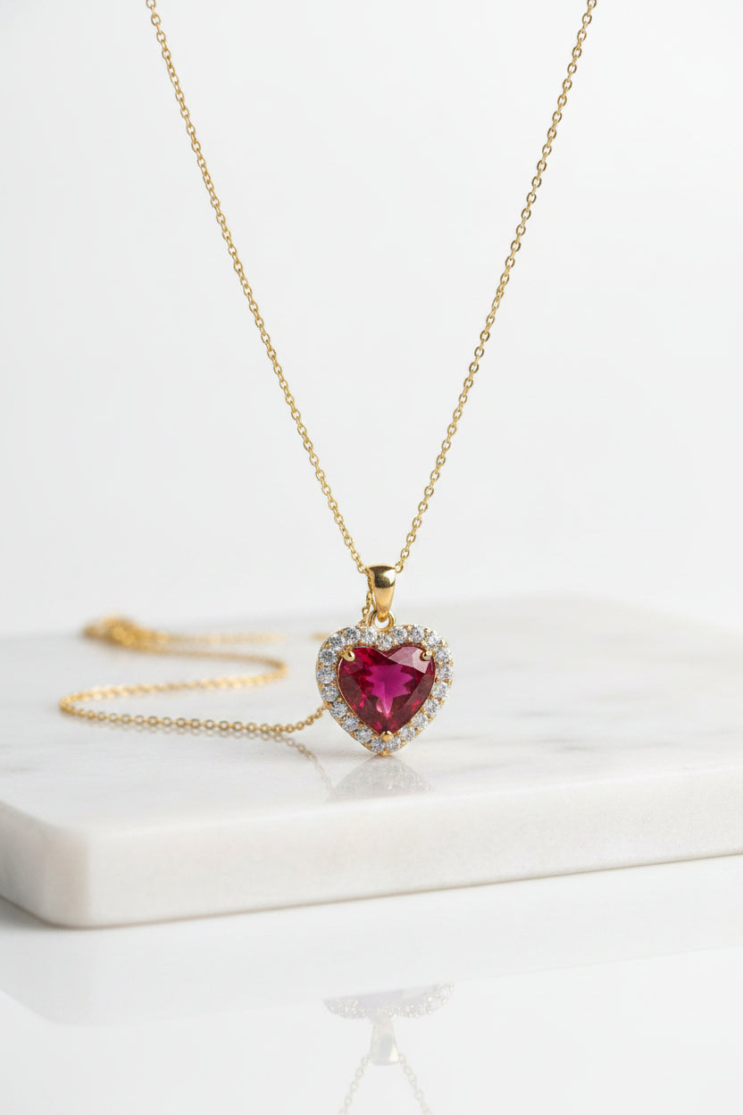 Gold necklace with a heart-shaped red gemstone pendant on a mannequin bust.