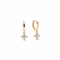A pair of gold hoop earrings with small flower charms set with clear stones, displayed on a beige velvet jewelry box.