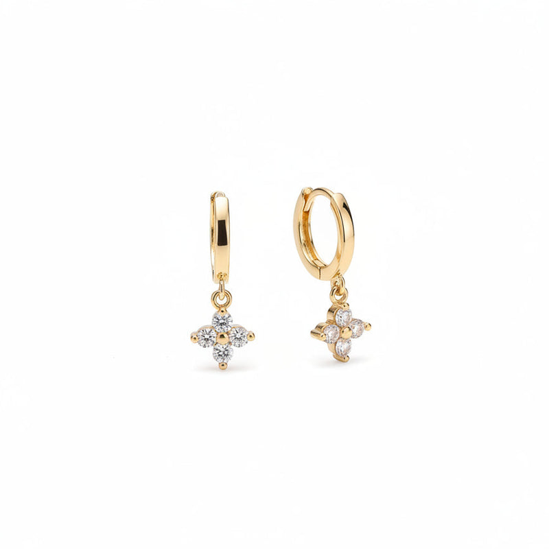 A pair of gold hoop earrings with small flower charms set with clear stones, displayed on a beige velvet jewelry box.