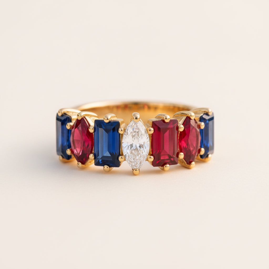 A gold ring featuring a row of marquise-cut gemstones in blue, white, and red, resting on a textured stone surface with a blurred natural background.