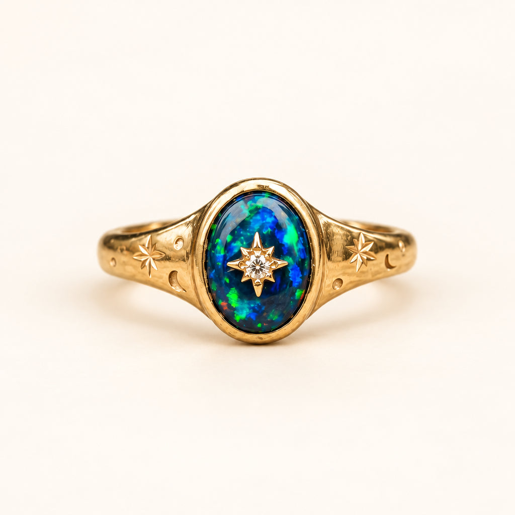A gold ring featuring an oval blue opal centerpiece with a small starburst motif in the middle, set on a rustic stone surface with a blurred natural background.