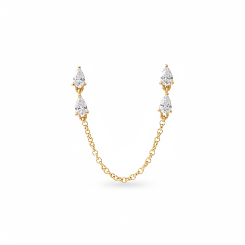 A pair of gold drop earrings with pear-cut clear stones and a connecting chain, presented in an open blue velvet jewelry box with the brand name AURORA FINE JEWELRY visible inside.