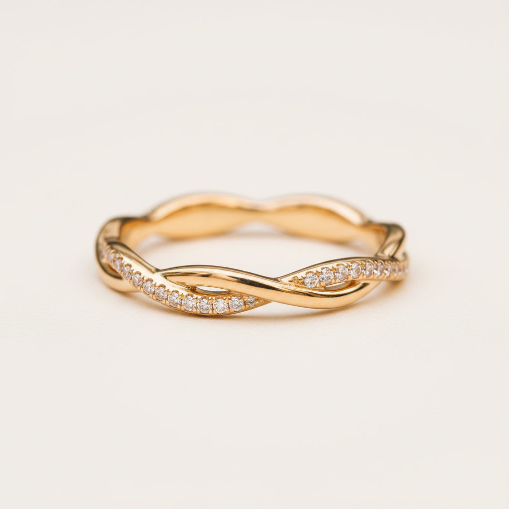 A gold twist ring with pavé-set clear stones, resting on a textured stone surface with a blurred natural background.