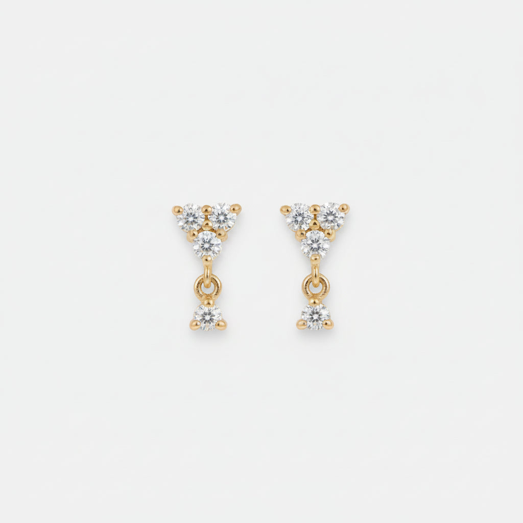 A pair of gold triangular dangle earrings with clear gemstones, resting on a draped beige satin fabric background.