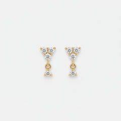 A pair of gold triangular dangle earrings with clear gemstones, resting on a draped beige satin fabric background.