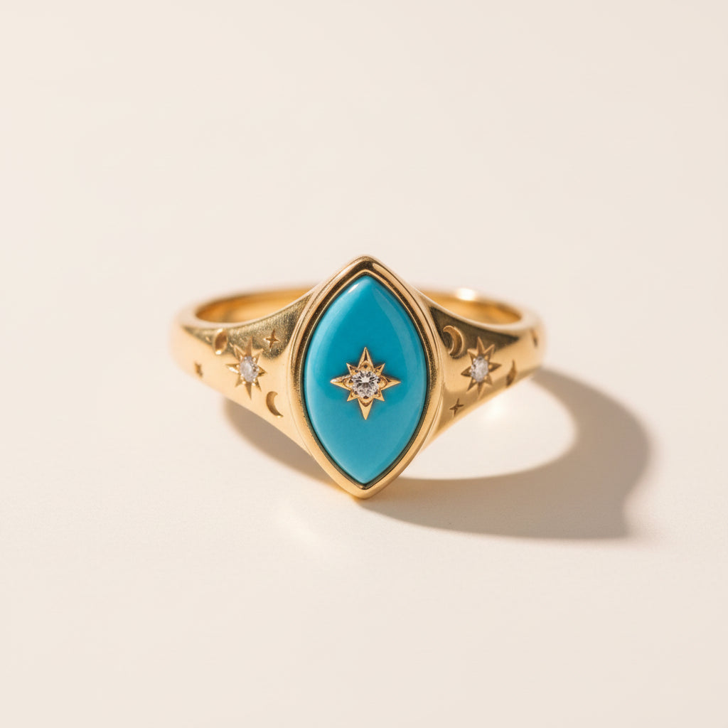 A gold ring with a marquise-shaped turquoise center stone and small star motifs, resting on a textured stone surface with a blurred natural background.