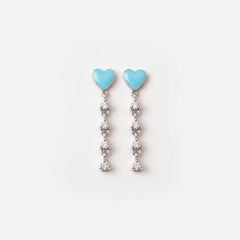 A pair of silver dangle earrings with light blue heart-shaped tops and clear rhinestone drops, displayed on a white ceramic plate.