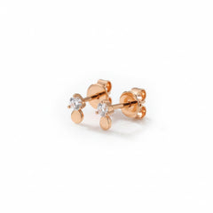 A pair of rose gold stud earrings with a small round clear gemstone and a flat circular drop, displayed on a white marble block.