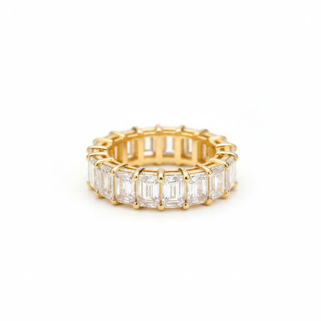 A gold eternity ring featuring baguette-cut clear gemstones, photographed on a textured brown surface.