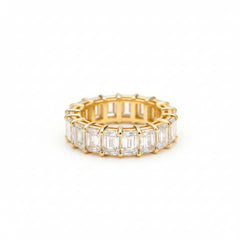 A gold eternity ring featuring baguette-cut clear gemstones, photographed on a textured brown surface.