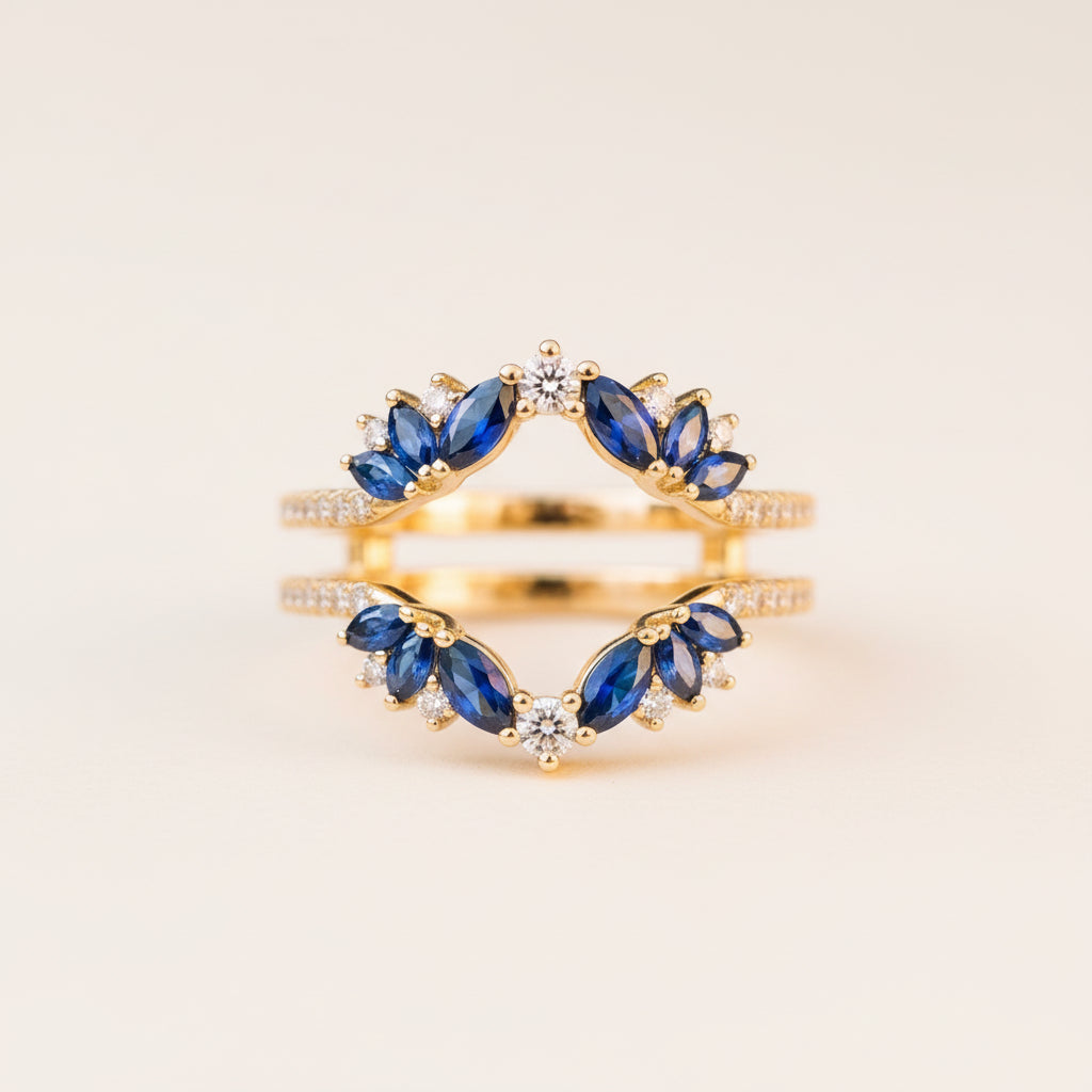 A pair of gold rings with marquise-cut blue gemstones and small clear accent stones, displayed on a textured stone surface with a blurred natural background.