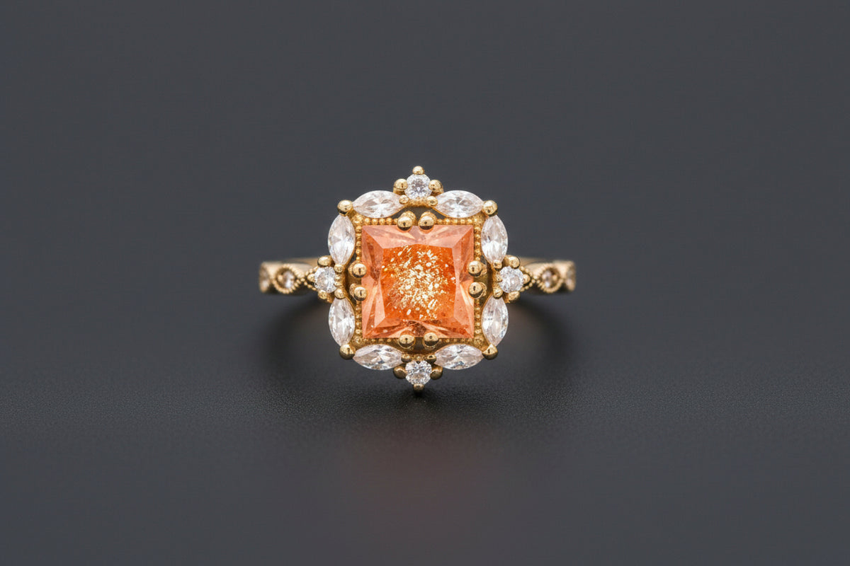 A yellow gold ring featuring a square orange center stone surrounded by clear marquise and round stones, resting on a textured stone surface with a blurred natural background.