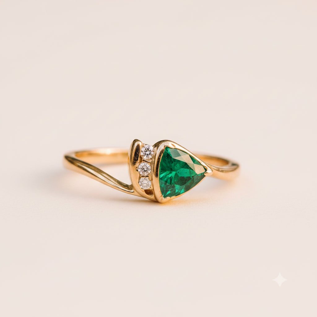 A gold ring with a triangular green emerald-cut center stone and small clear accent stones, resting on a textured stone surface with a blurred natural background.