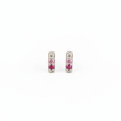 A pair of silver-toned rectangular stud earrings with pink gemstones, resting on a textured piece of weathered wood.