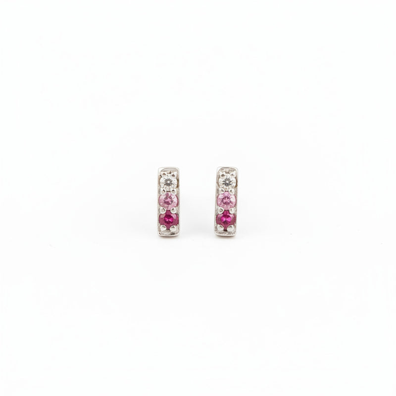 A pair of silver-toned rectangular stud earrings with pink gemstones, resting on a textured piece of weathered wood.
