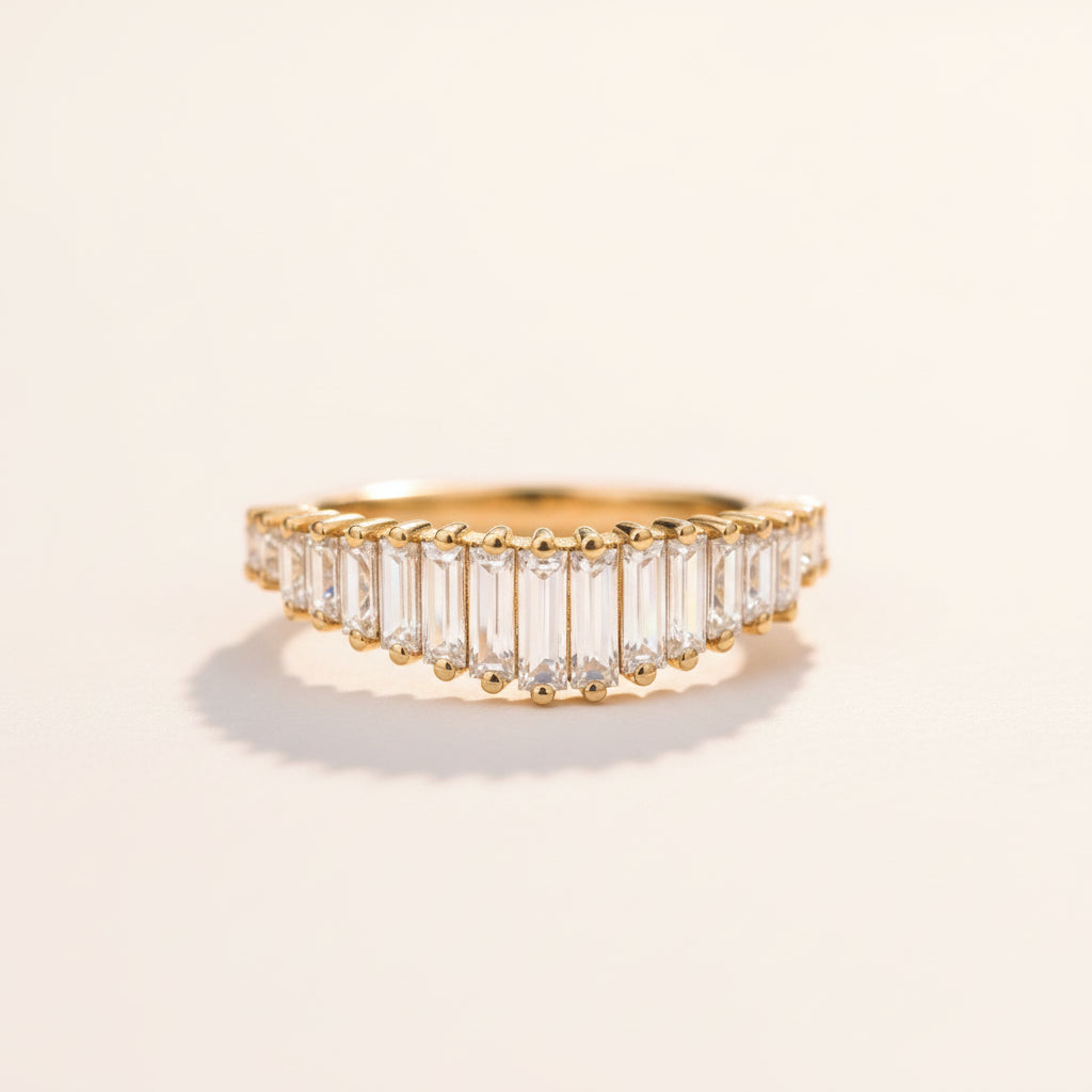 A gold eternity ring featuring baguette-cut clear stones, resting on a textured stone surface with a soft-focus natural background.