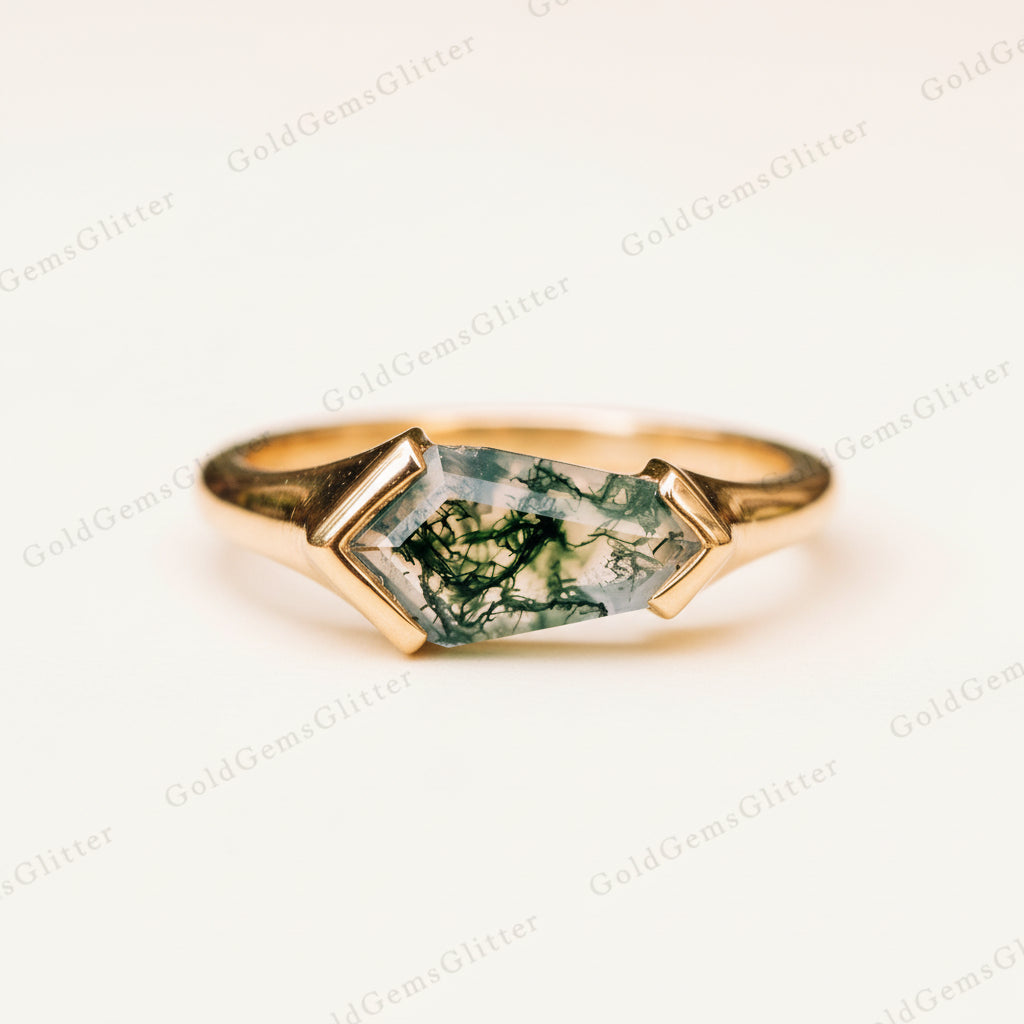 A gold ring featuring a marquise-cut green jasper gemstone with natural inclusions, resting on a textured stone surface with a blurred natural background.
