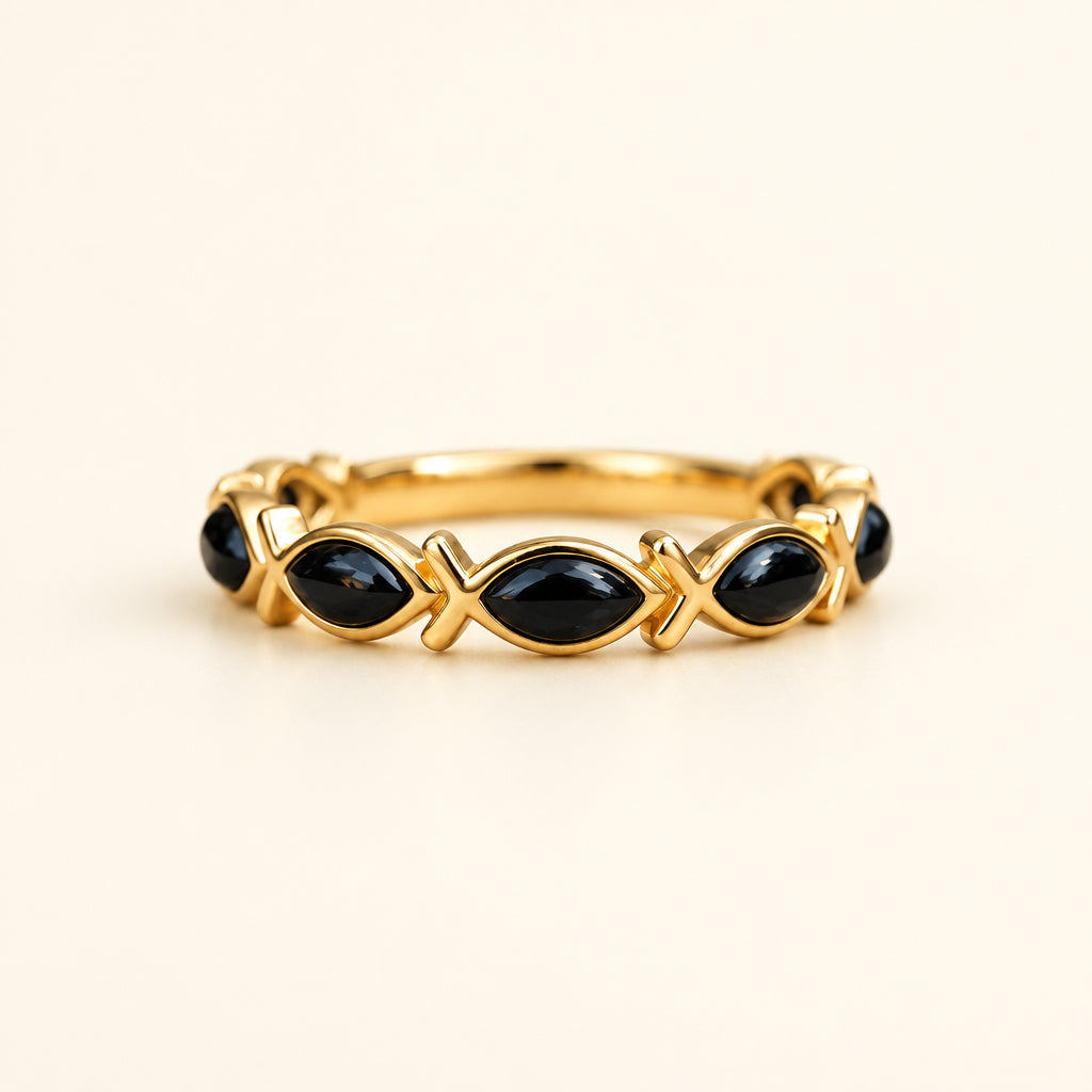 A gold bangle bracelet with black onyx fish motifs, resting on a textured stone with a blurred green garden background.