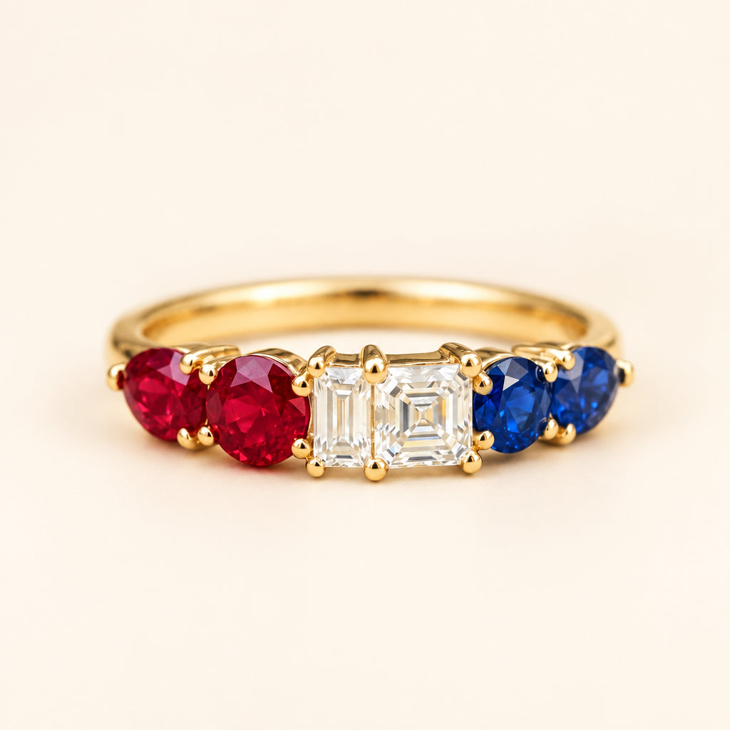 A gold ring featuring a central baguette-cut clear gemstone, flanked by a red marquise-cut gemstone on the left and a blue round-cut gemstone on the right, resting on a textured stone surface.