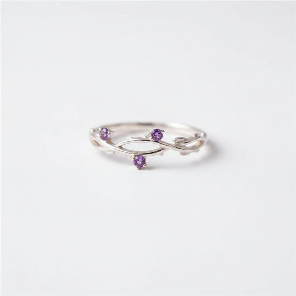 A silver ring with three small purple gemstone accents, displayed on a black velvet-lined wooden jewelry box.