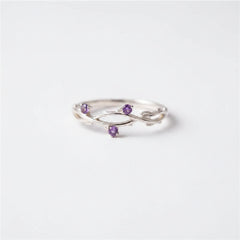 A silver ring with three small purple gemstone accents, displayed on a black velvet-lined wooden jewelry box.