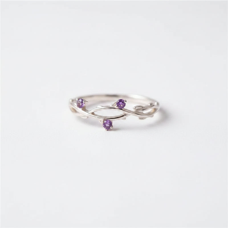 A silver ring with three small purple gemstone accents, displayed on a black velvet-lined wooden jewelry box.