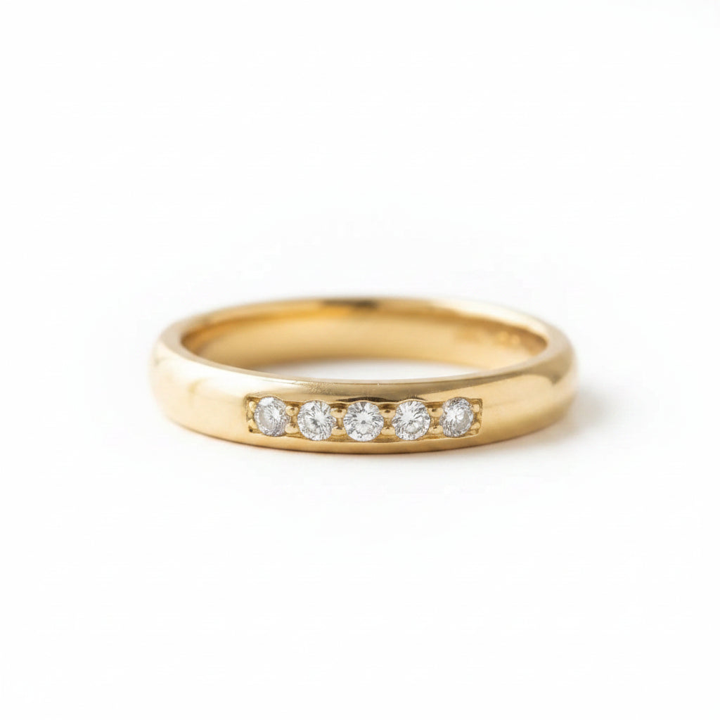A yellow gold eternity ring with five round-cut clear gemstones set in a row, resting on a textured blue velvet surface.