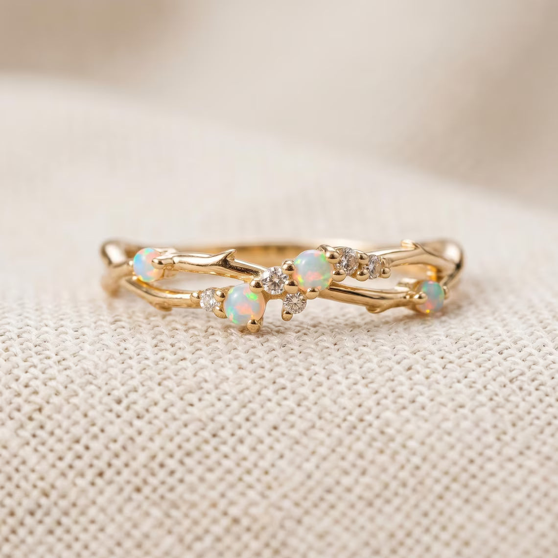 A gold branch-style ring with small white opal and clear crystal accents, photographed close-up on a textured cream fabric background.