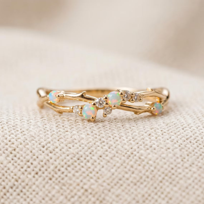 A gold branch-style ring with small white opal and clear crystal accents, photographed close-up on a textured cream fabric background.